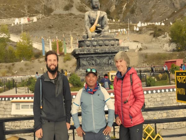 Three-trekkers-posing-in-front-of-a-large-Buddha-statue-in-the-Himalayas